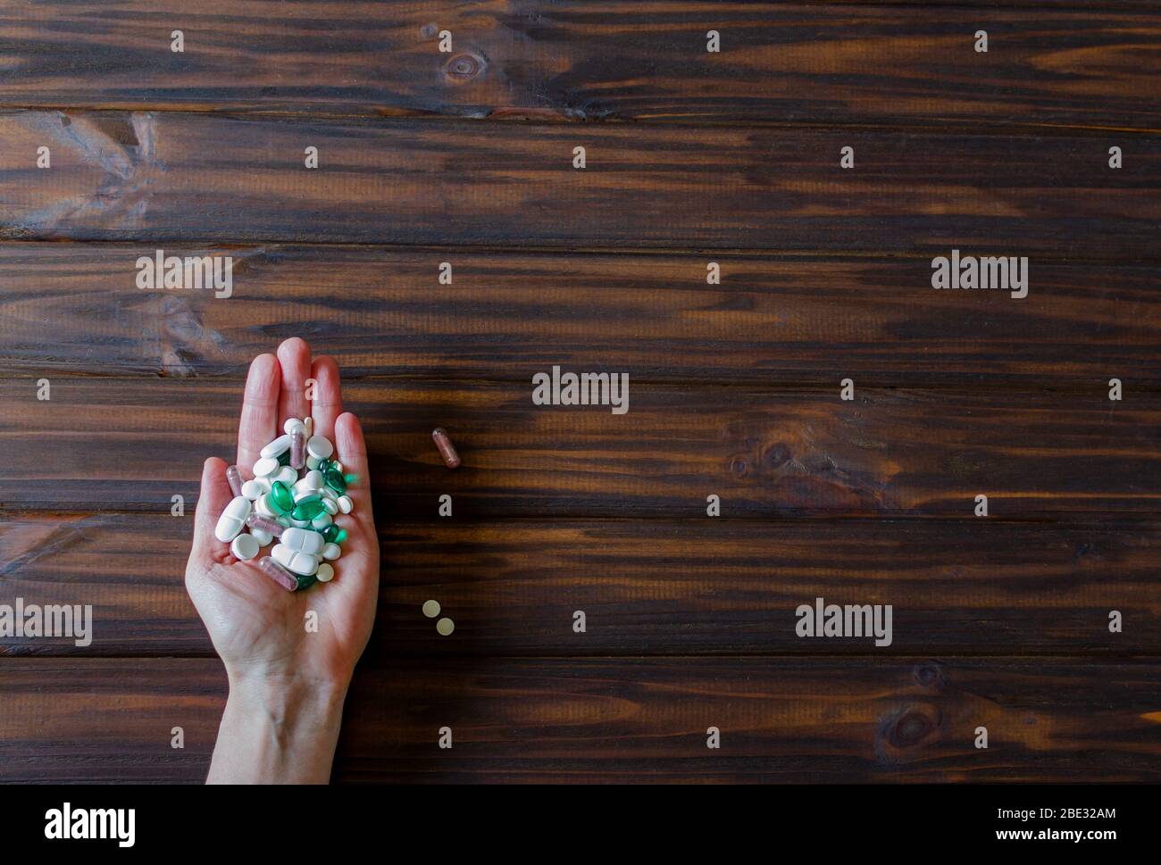 Eine Menge von farbigen Pillen in der Hand einer Frau auf Holzhintergrund. Gesundheitskonzept und medizinisches Konzept. Horizontaler Rahmen mit freiem Platz für Text. Stockfoto