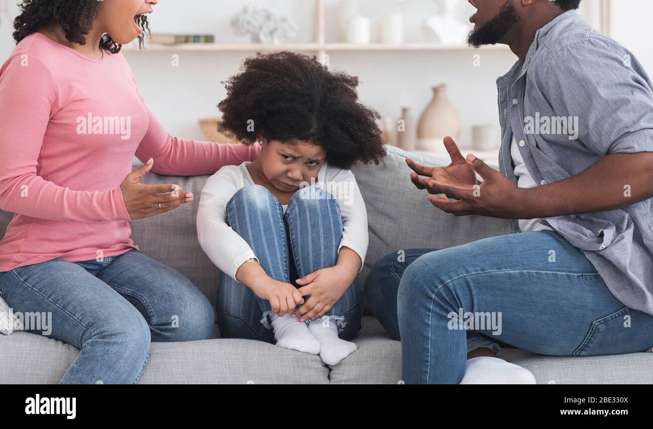 Arme Kleine Schwarze Mädchen Sitzt Auf Der Couch Zwischen Streitbaren Erwachsenen Stockfoto