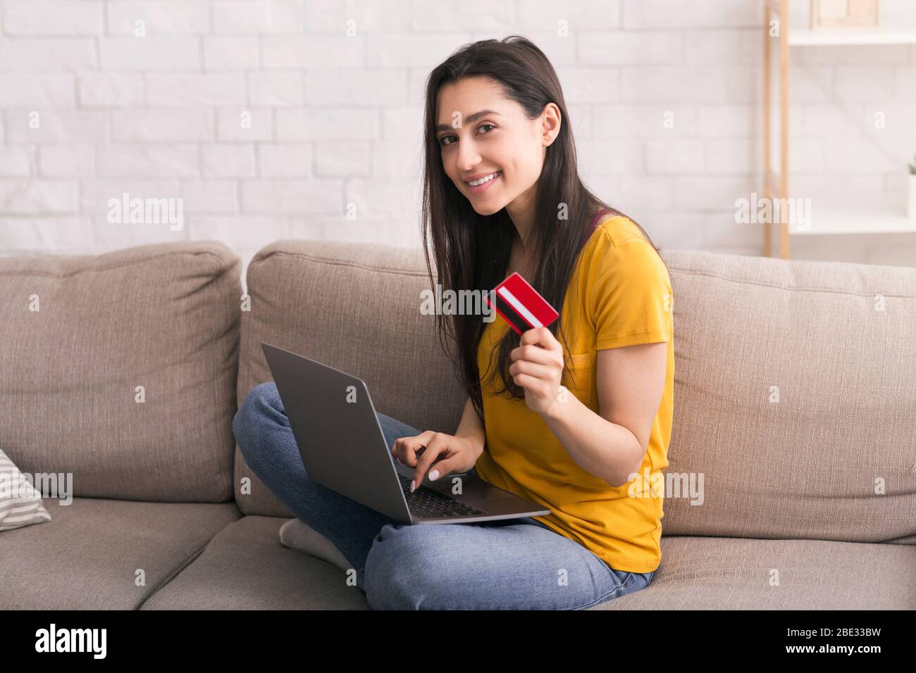 COVID-19 Lockdown Shopping. Schönes Mädchen mit Laptop und Bankkarte etwas über das Internet zu Hause kaufen Stockfoto