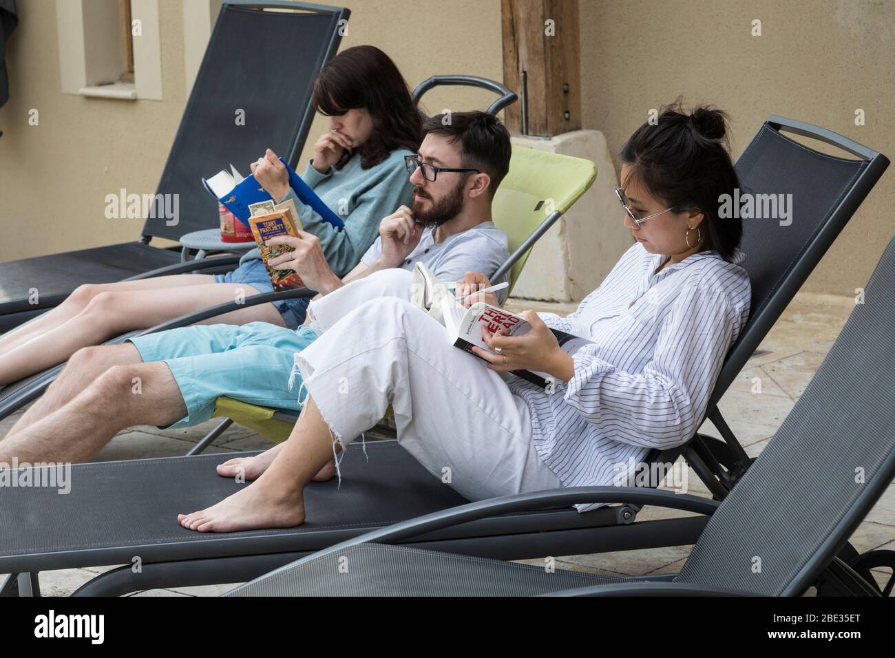 Zwei Frauen und ein Mann entspannen sich auf den Liegen beim Lesen von Büchern. Stockfoto