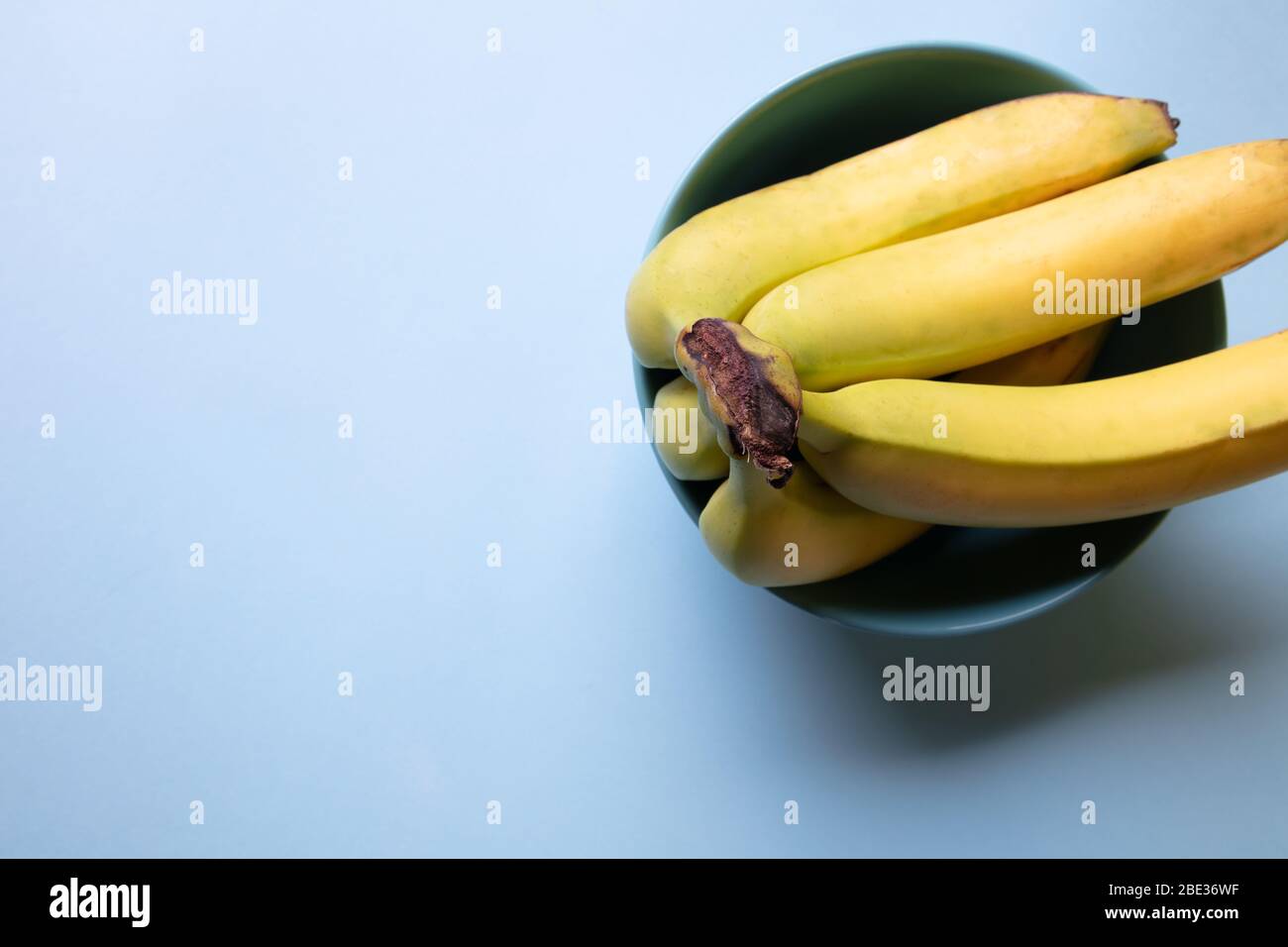 Ein frischer Blick auf einen Haufen Bananen, die in einer hellblauen Schüssel mit einem pastellfarbenen hellblauen Hintergrund ruhen, Draufsicht Stockfoto