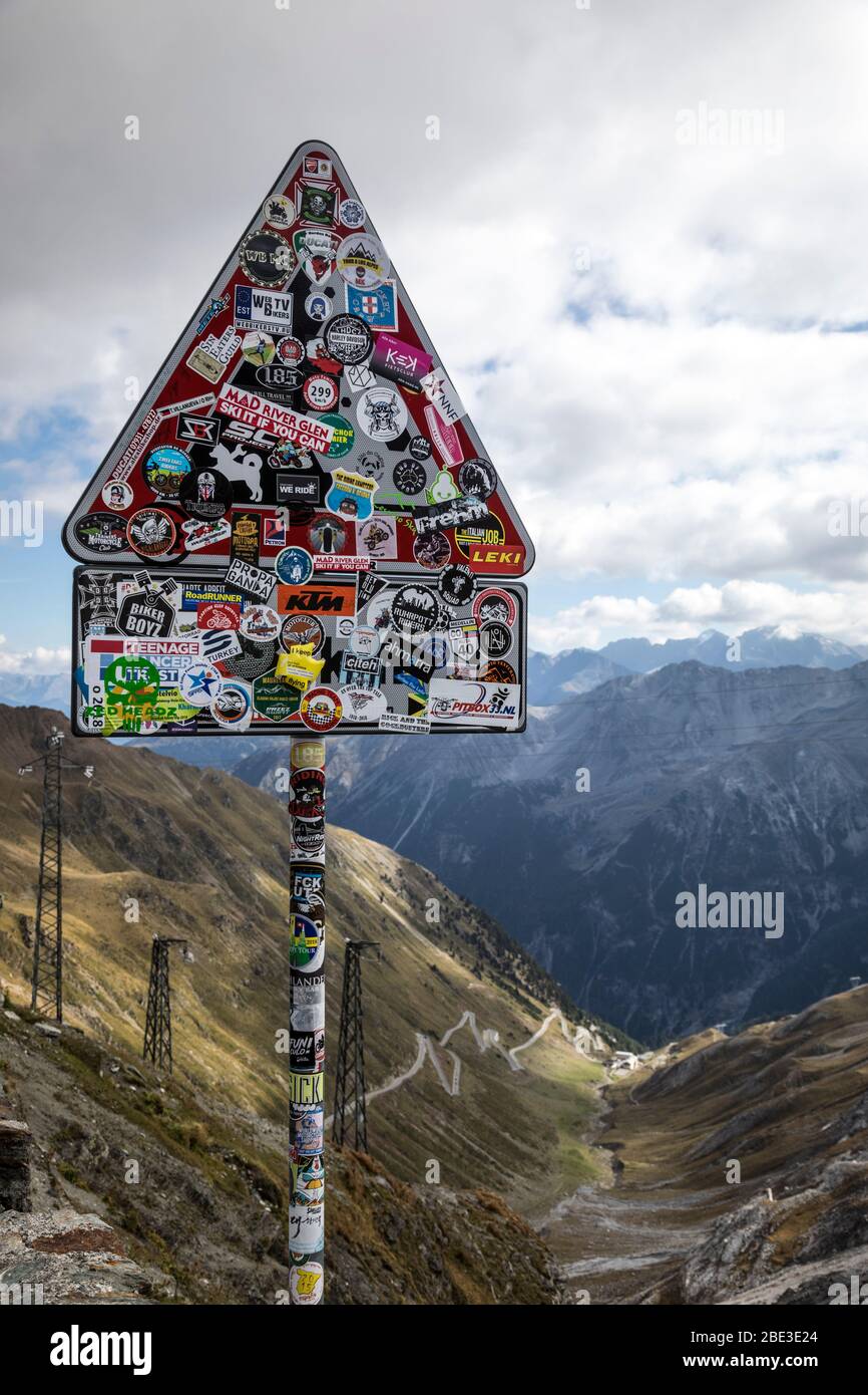 Die Rückseite eines mit Stickern bedeckten Wegschildes auf dem Gipfel des Stilfserjochs, das seine vielen Kehren zeigt, Italien. Stockfoto