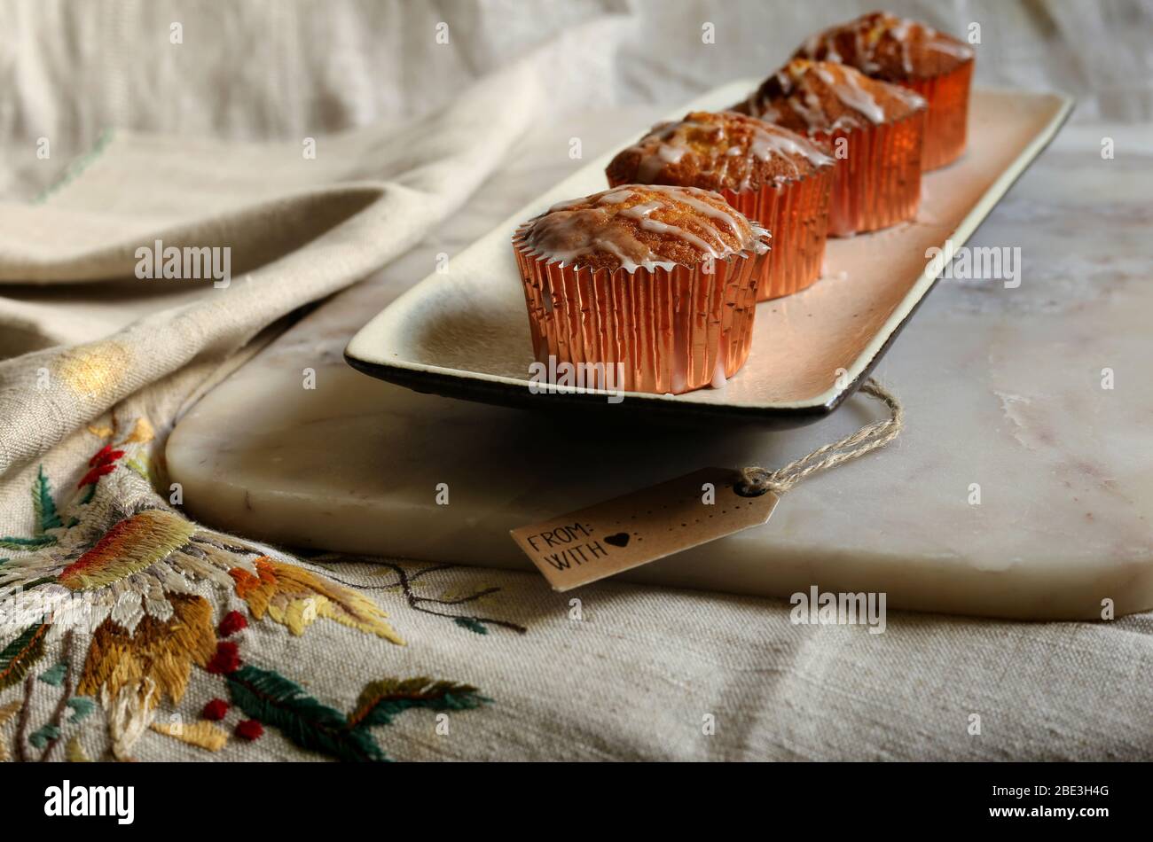Hausgemachte frische köstliche Tasse Kuchen auf weißem Teller auf Marmor oben auf Leinwand mit Geschenk-Tag mit Zeichen mit Liebe. Grüne Pflanze auf Hintergrund. Stockfoto