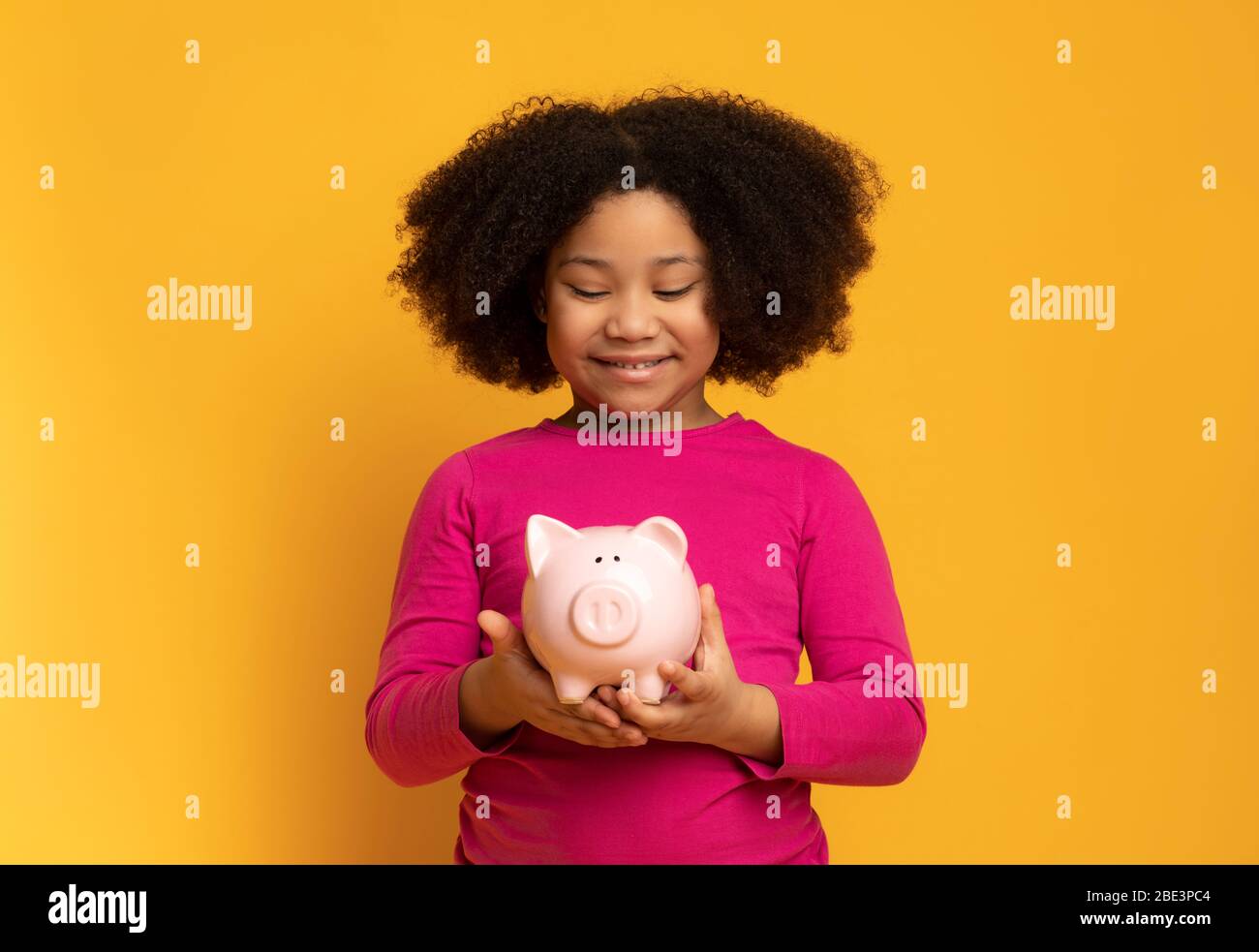 Kluge Einsparungen. Liebenswert Kleine Afro Mädchen Holding Piggy Bank In Händen, Stockfoto