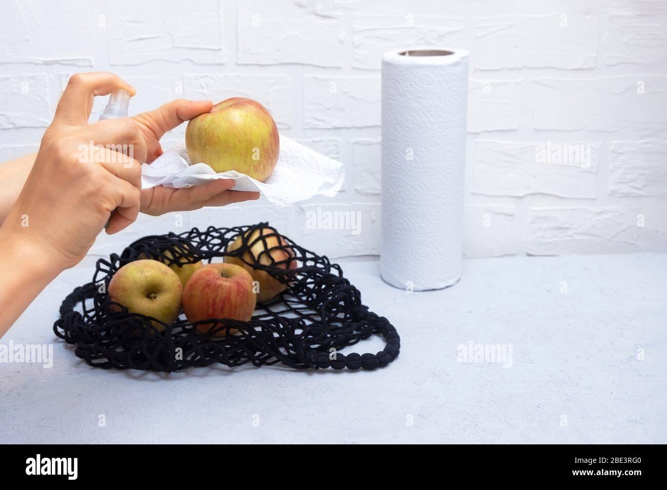 Frauenhände halten Desinfektionsmittel und reinigen Lebensmittel in der Küche mit Netzbeutel auf Hintergrund. Coronavirus Konzept für Lebensmittelsicherheit Stockfoto