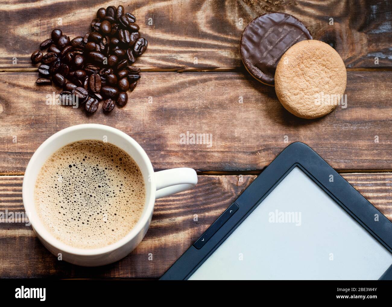 Kaffe mit Schaum, Ebook, Kuchen, herzförmige Kaffeebohnen auf dem Holztisch. Flach lag ohne Leute Stockfoto