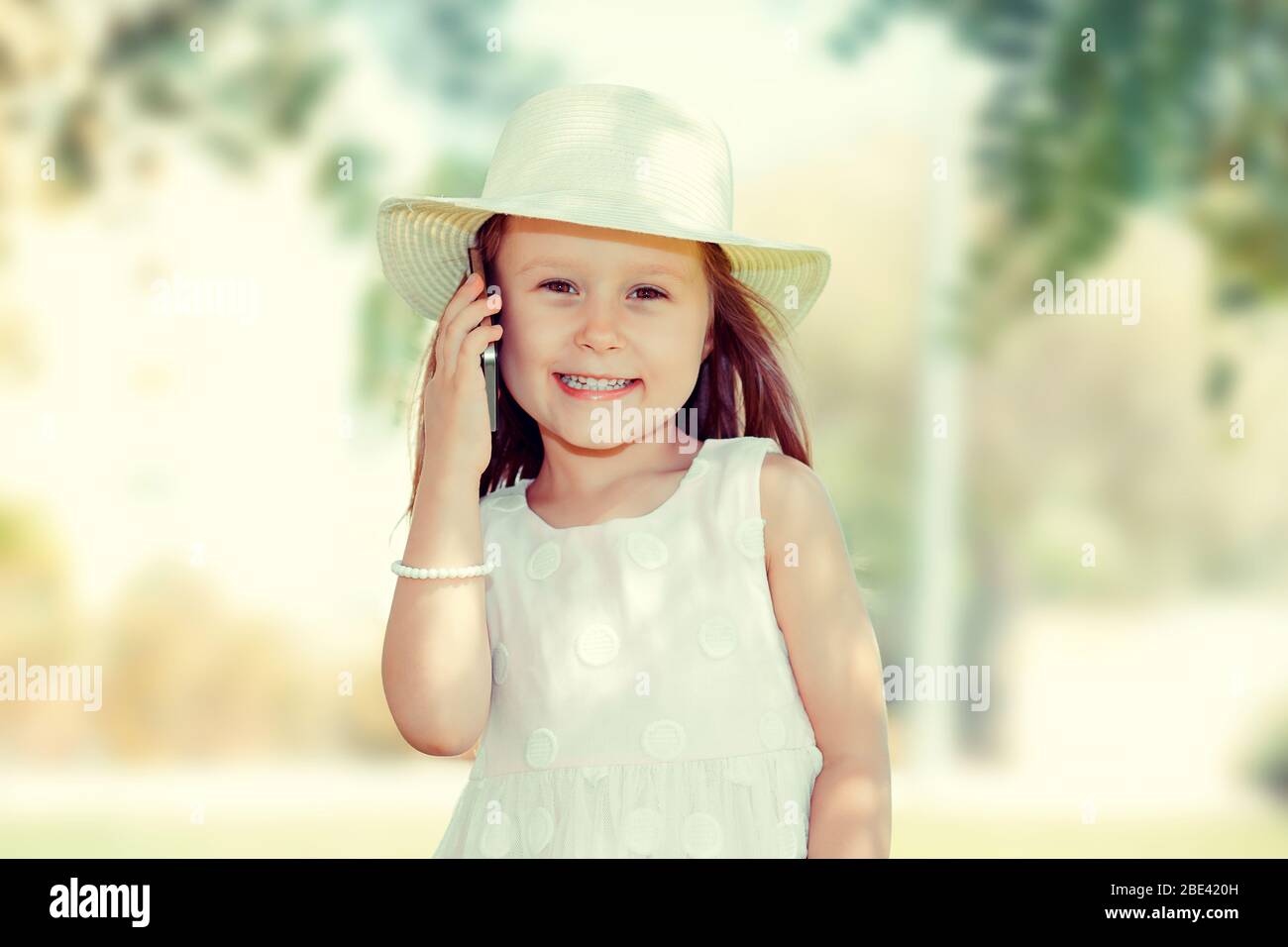 Kind mit Smartphone. Nahaufnahme Porträt von ziemlich lächelnd lustige Mädchen Kind hält Handy sprechen mit ihrer Mutter, Papa Familie isoliert grünen Bäumen im Freien Stockfoto