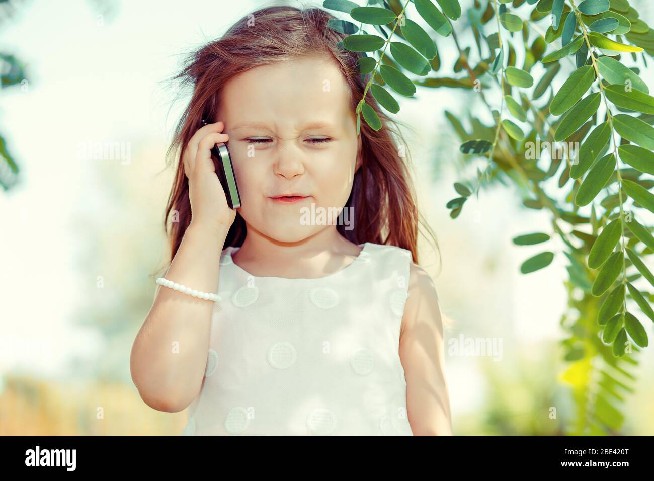 Kids & Technology Konzept. Nahaufnahme Porträt Kopfschuss der schönen aufgeregt unglücklich, ernst kleines Mädchen reden auf mobilen grünen Park im Freien Hintergrund. Stockfoto
