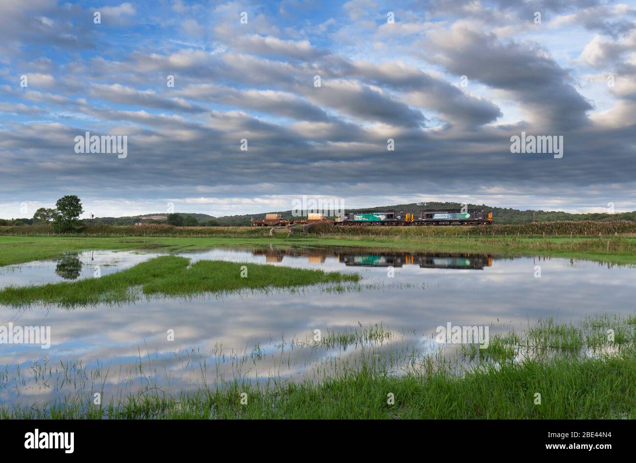 2 Direct Rail Services Lokomotiven der Baureihe 37 auf der Küstenbahnlinie Cumbria mit einem Kernflastenzug, der sich in einem überfluteten Feld widerspiegelt Stockfoto