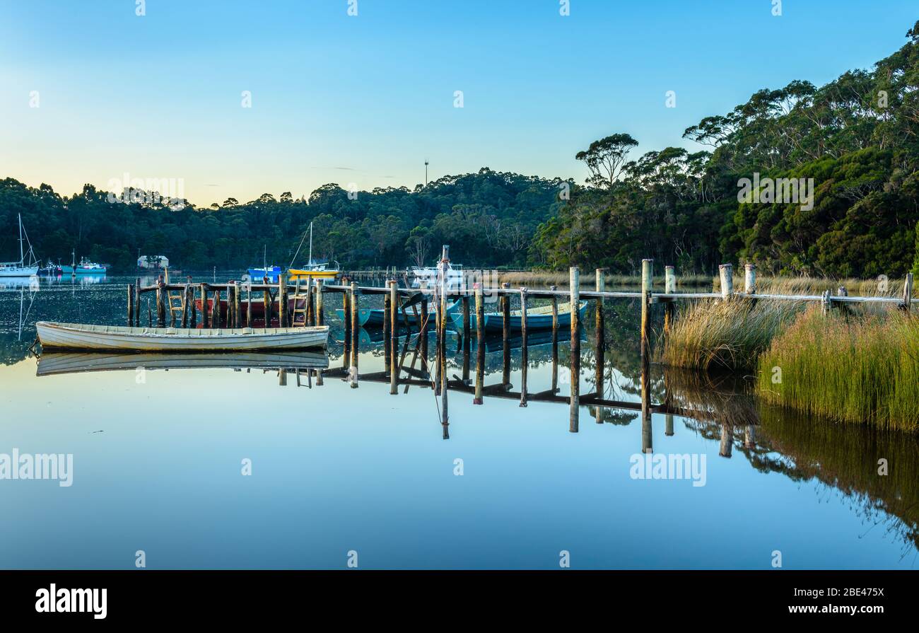 Traditionelle Holzboote liegen an einem Holzsteg am Macquarie Harbour, im Hintergrund liegt die Stadt Strahan über der Bucht. Stockfoto