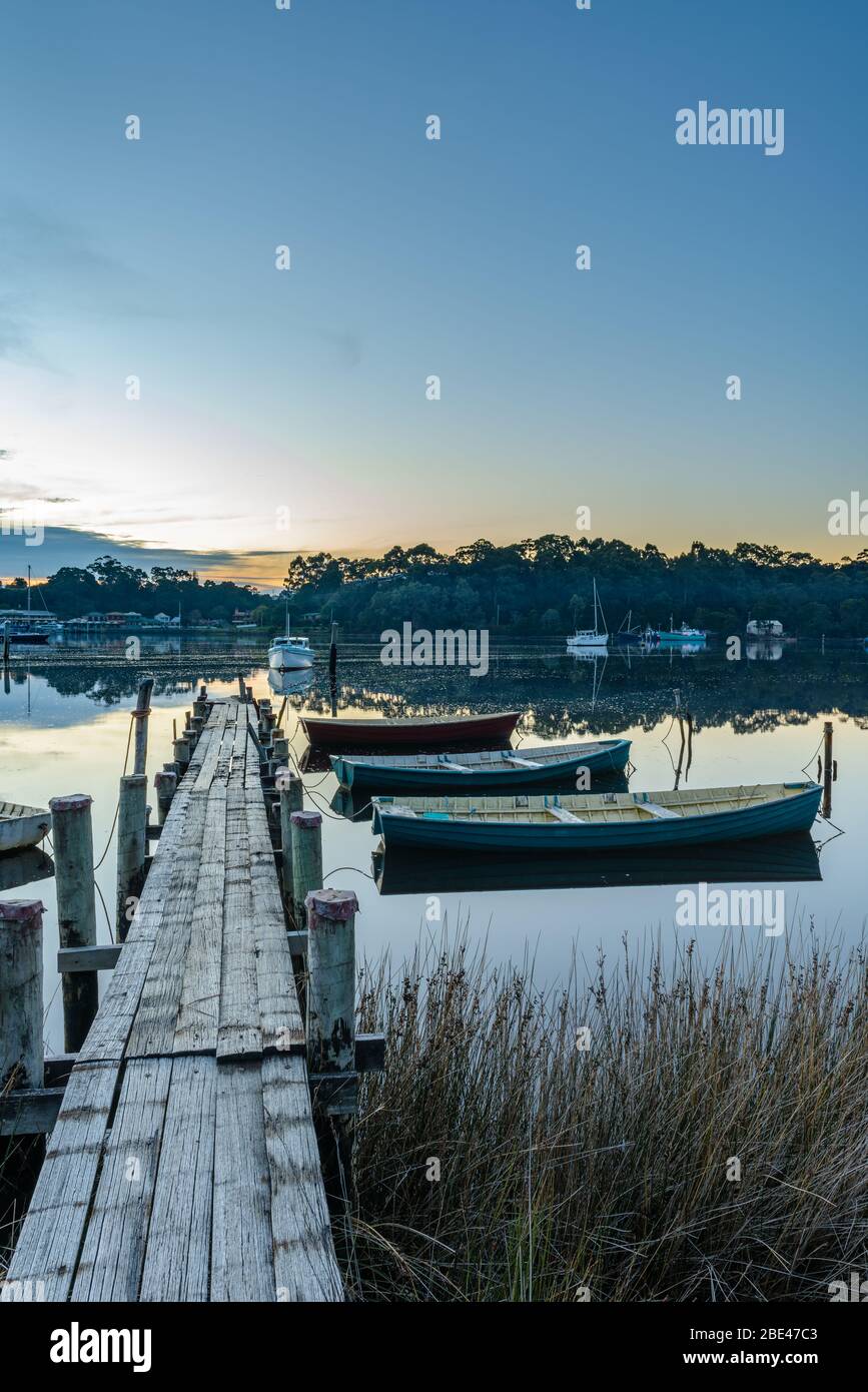 Traditionelle Holzboote liegen an einem Holzsteg am Macquarie Harbour, im Hintergrund liegt die Stadt Strahan über der Bucht. Stockfoto