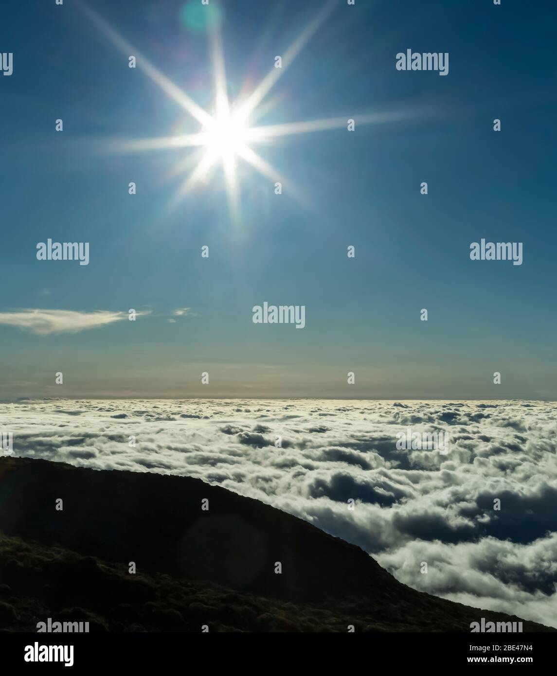 Sunburst im blauen Himmel über den Wolken, East Maui Volcano (Haleakala) bei Sonnenuntergang, Maui, Hawaii, Vereinigte Staaten von Amerika Stockfoto