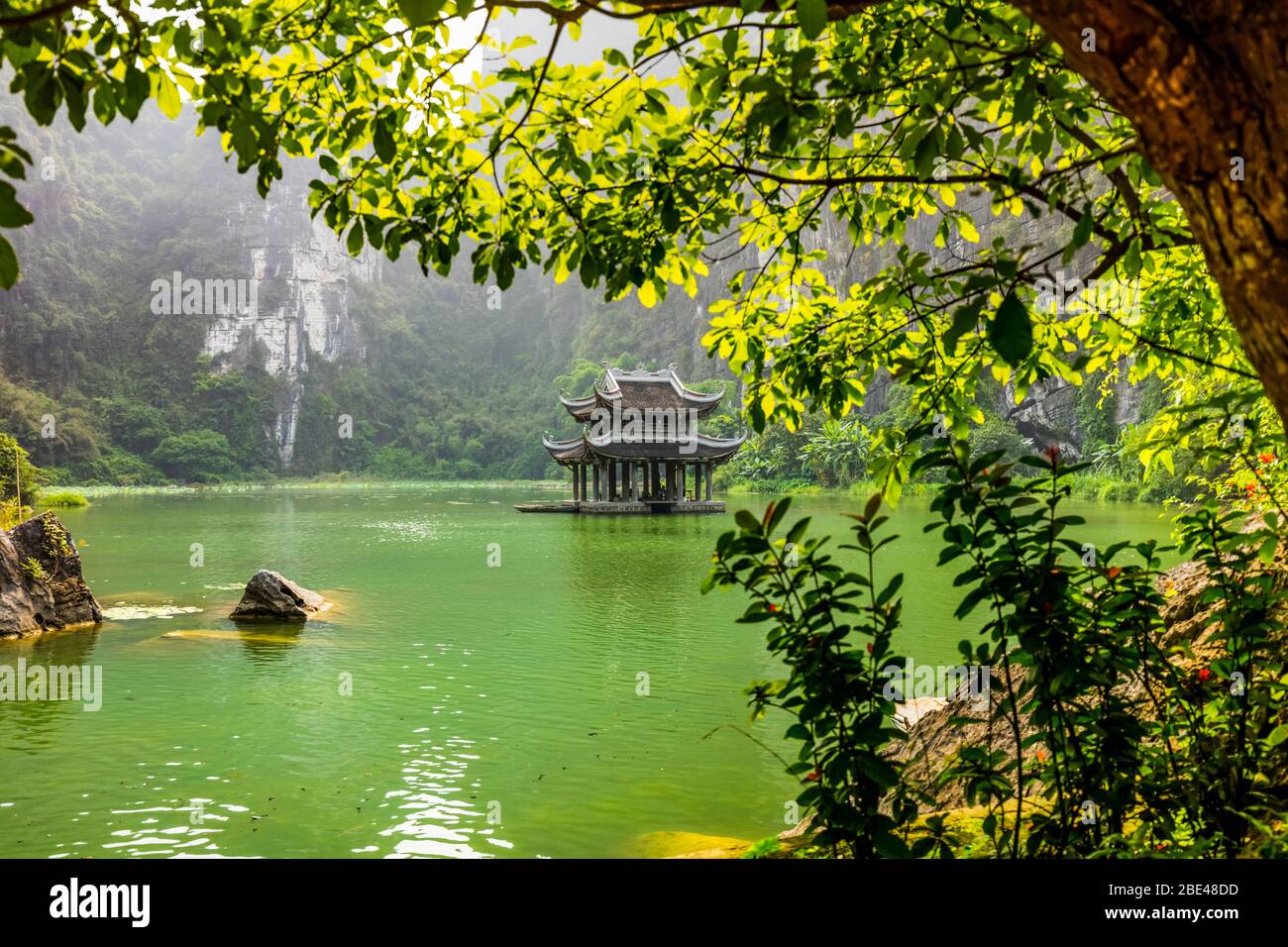 Üppige Landschaft und eine traditionelle asiatische Struktur in der Mitte eines grünen Sees; Ninh Binh Provinz, Vietnam Stockfoto