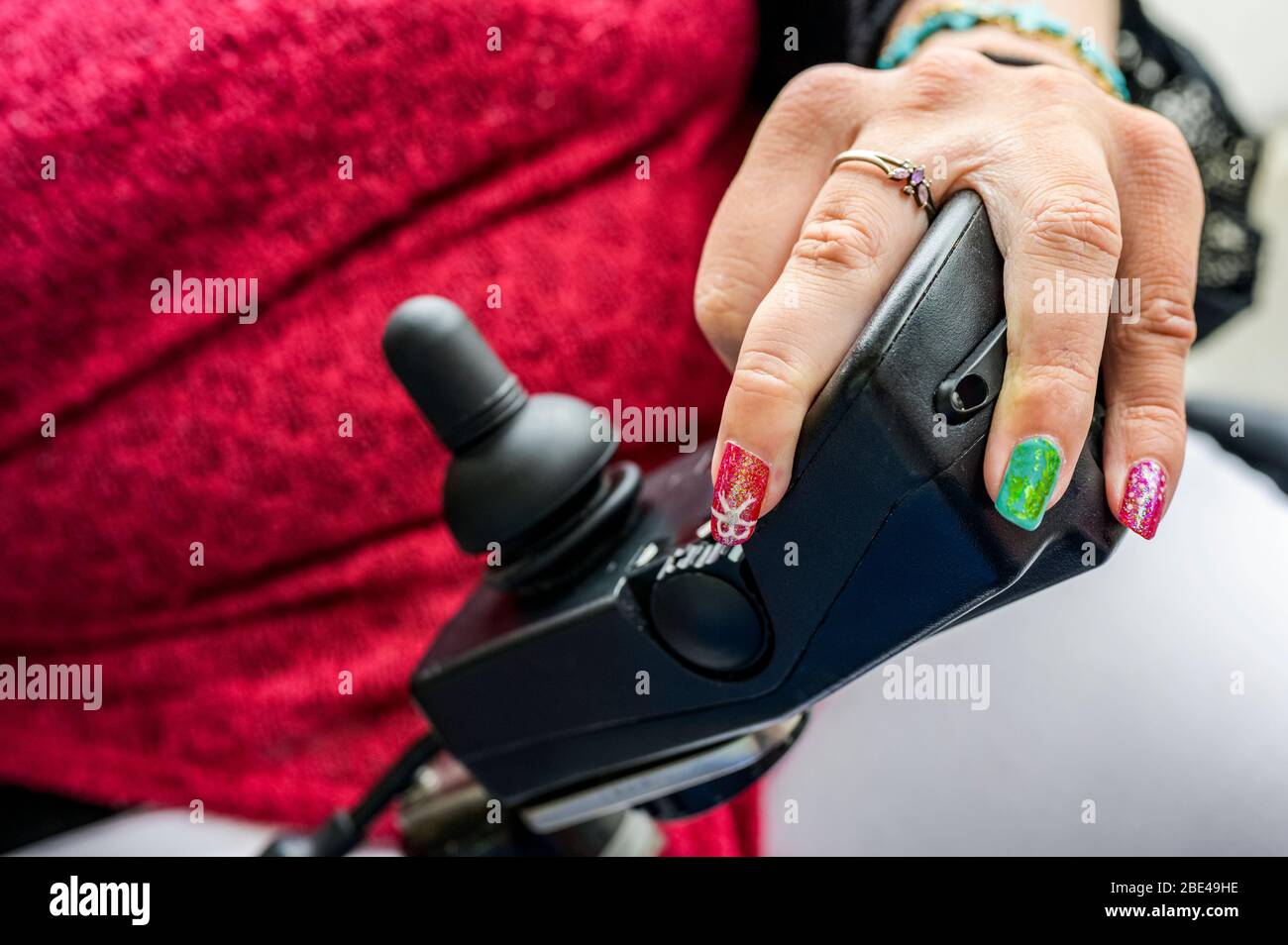 Maori Frau mit Zerebralparese in einem elektrischen Rollstuhl mit Joystick und Controller, Fingernägel mit Nail Art; Wellington, Neuseeland Stockfoto