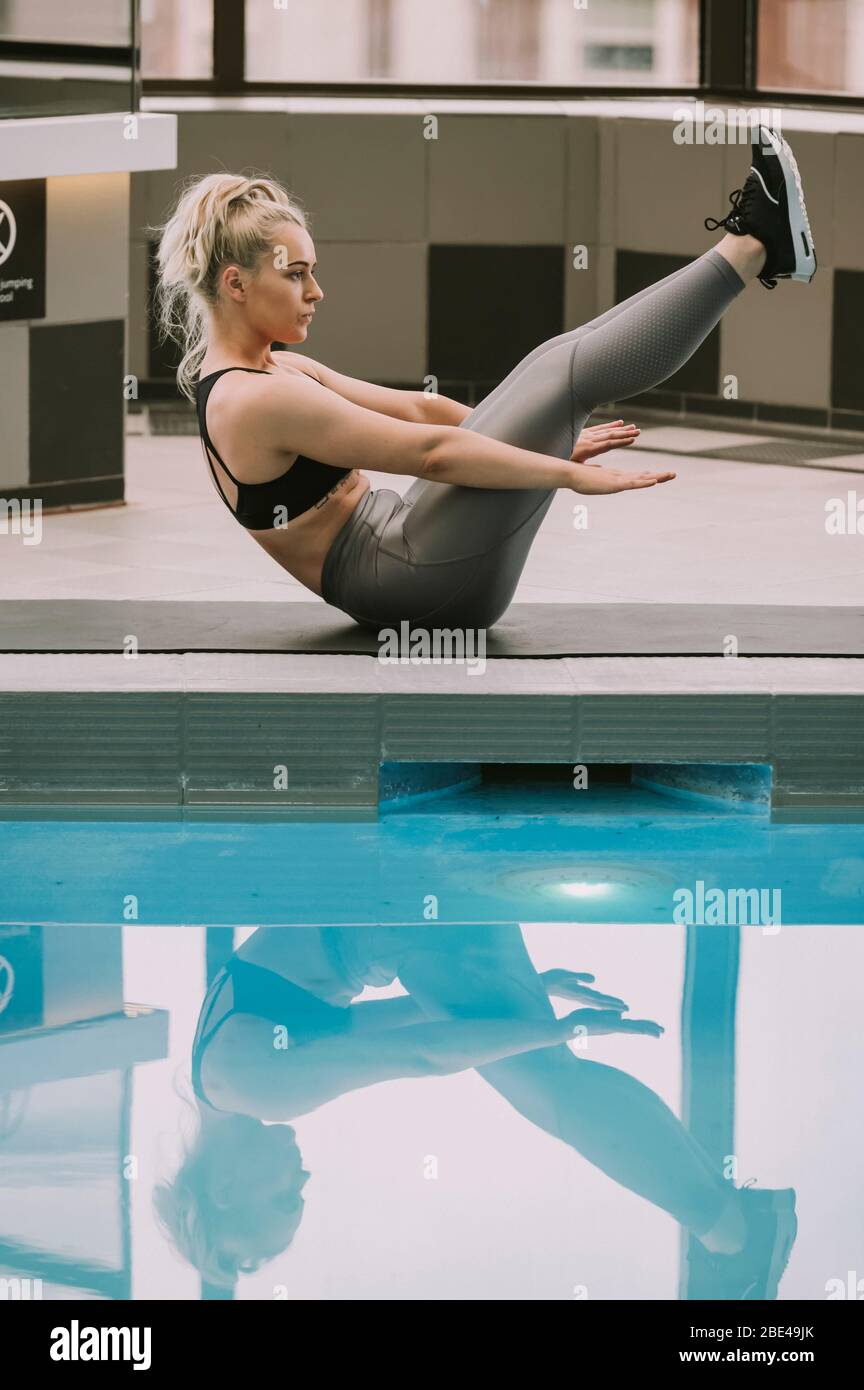Frau, die auf einer Matte trainiert und neben einem Pool eine Bauchübung macht; Wellington, Neuseeland Stockfoto