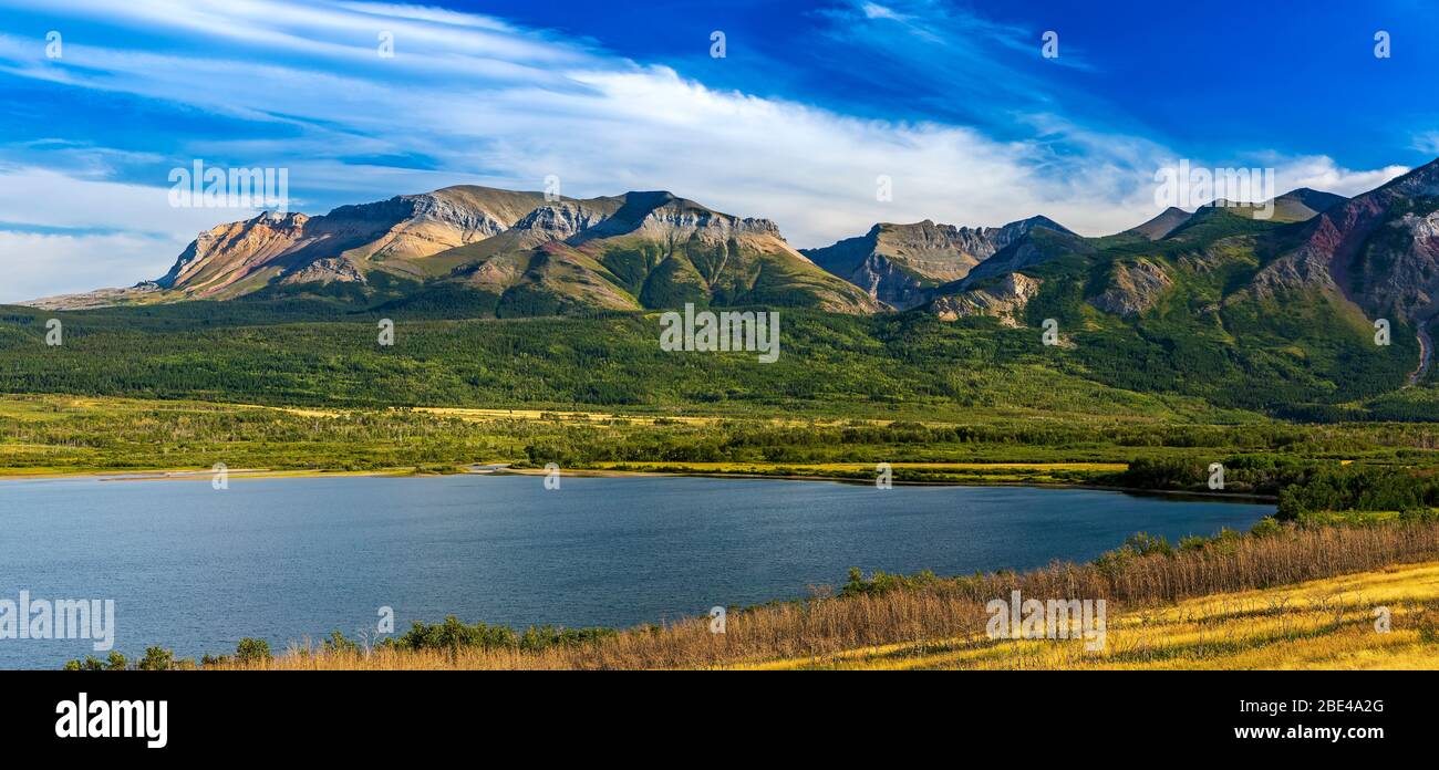 Panorama der Bergkette entlang eines Seeufers mit blauem Himmel und Wolken, Waterton Lakes National Park; Waterton, Alberta, Kanada Stockfoto