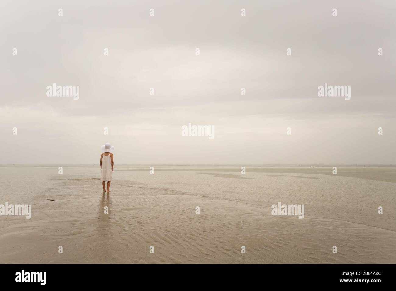 Junges Mädchen an einem Strand im Regen, das von der Kamera weg zeigt. Inspirierender Hintergrund mit Kopierbereich ideal für Angebote Stockfoto