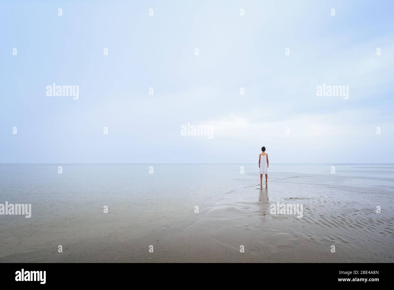 Junges Mädchen an einem Strand im Regen, das von der Kamera weg zeigt. Inspirierender Hintergrund mit Kopierbereich ideal für Angebote Stockfoto