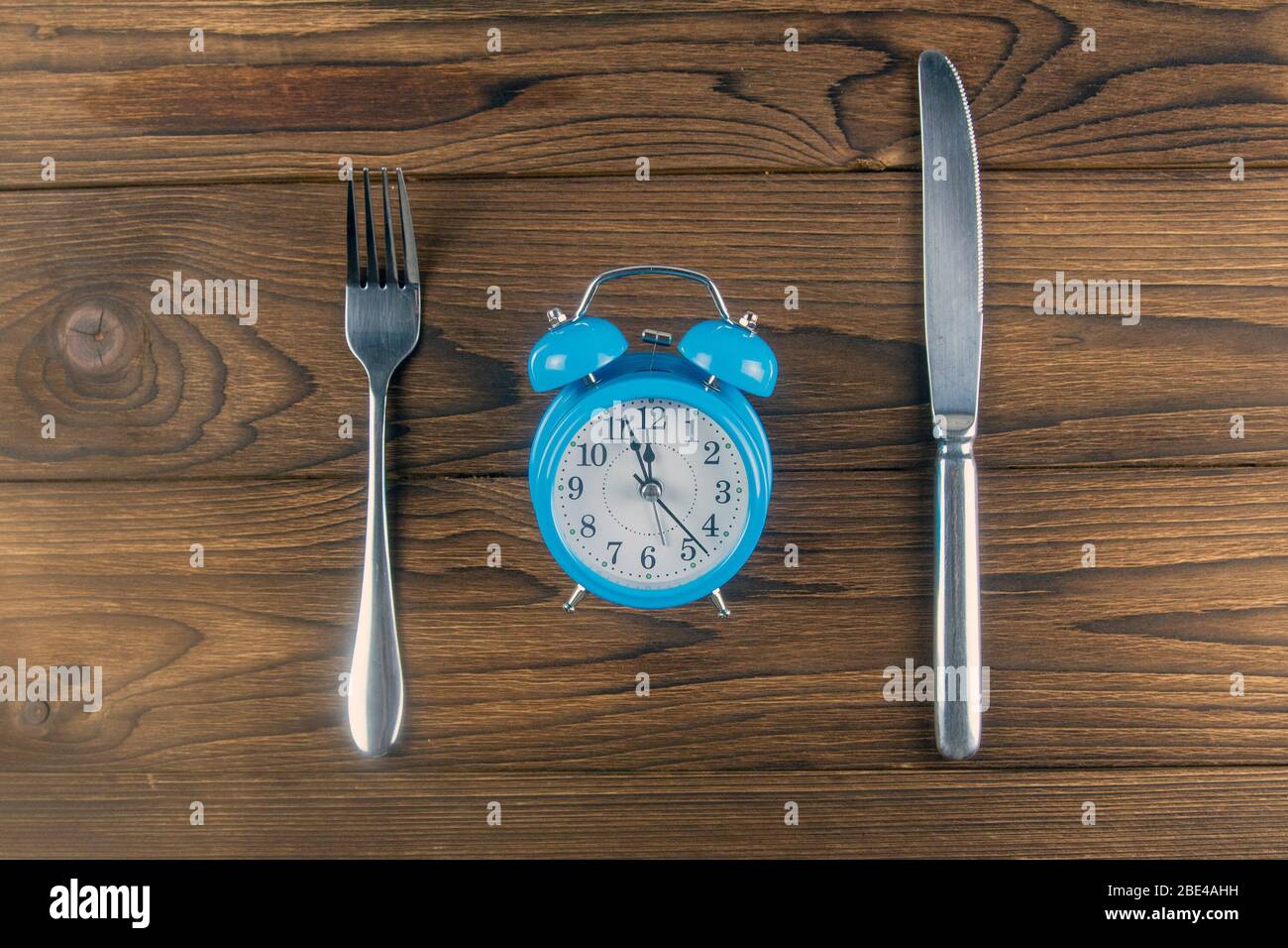 Eine Vintage Uhr mit Gabel und Messer auf dunklem Holz Tischansicht. Vintage-Farbton. Von oben Stockfoto