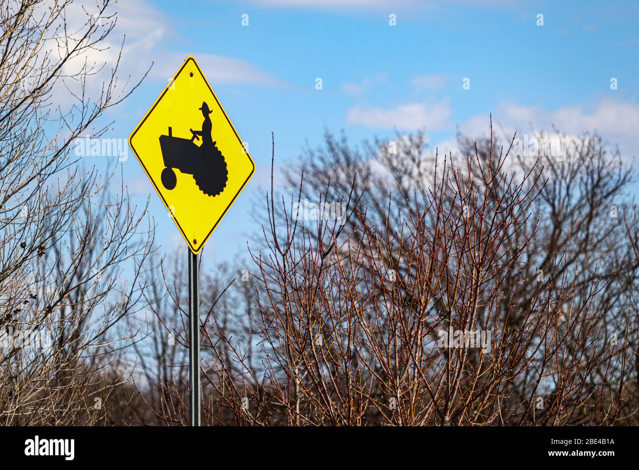 Ein gelbes Schild zeigt eine schwarze Abbildung eines Bauern, der auf einem Traktor fährt und einen gemeinsamen Traktorübergang auf einer Straße durch Ackerland markiert. Stockfoto