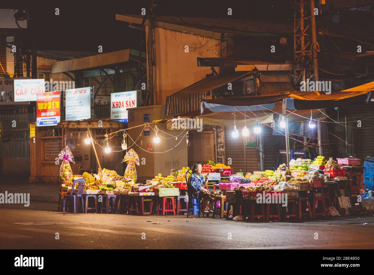 Eine ältere Verkäuferin sitzt mit ihrem Handy auf einem Nachtmarkt; Ho Chi Minh City, Vietnam Stockfoto