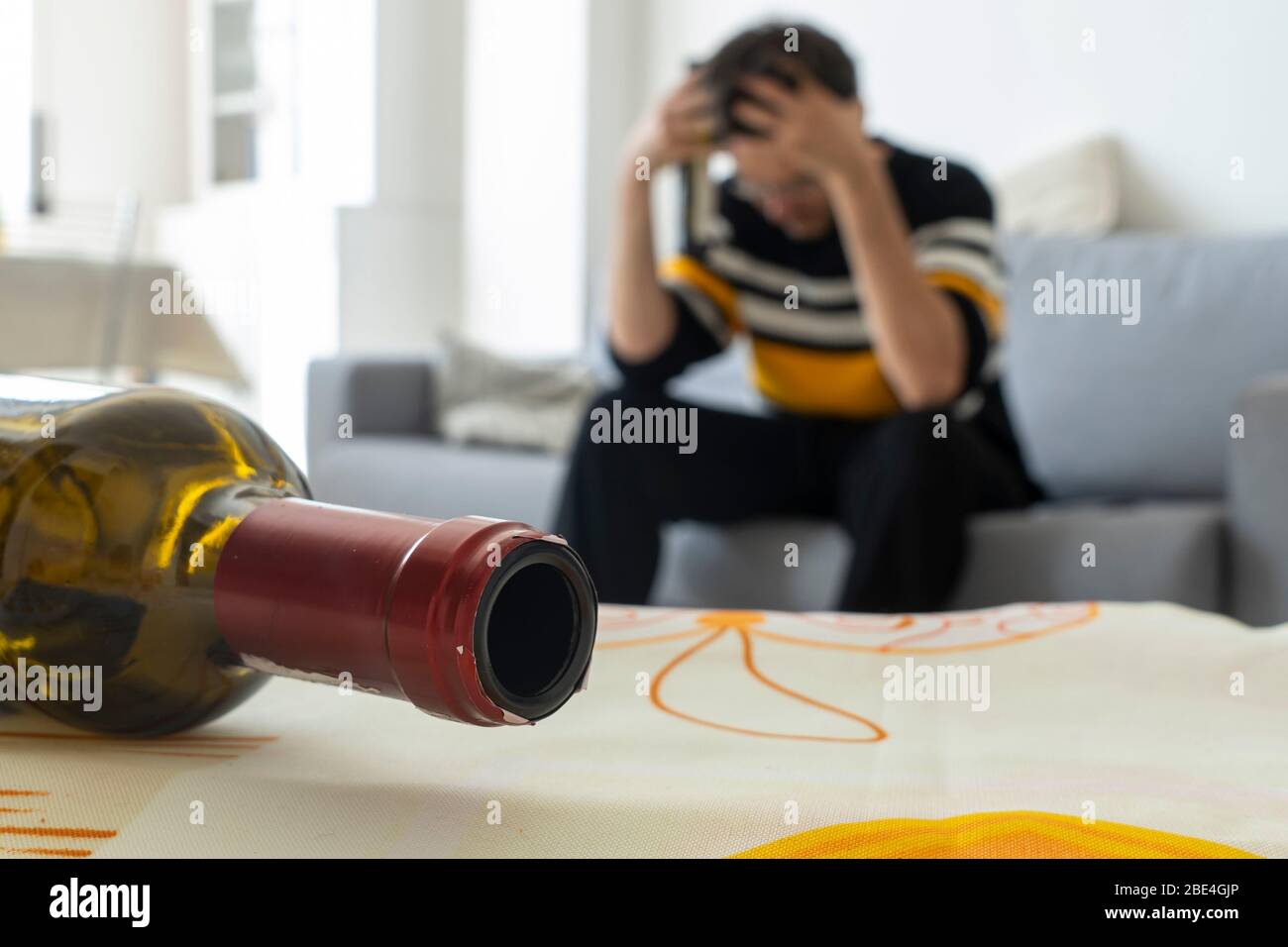 Alkoholiker verzweifelt auf dem Sofa zu Hause. Leere Flasche Wein im Vordergrund. Konzept der Alkoholsucht. Stockfoto