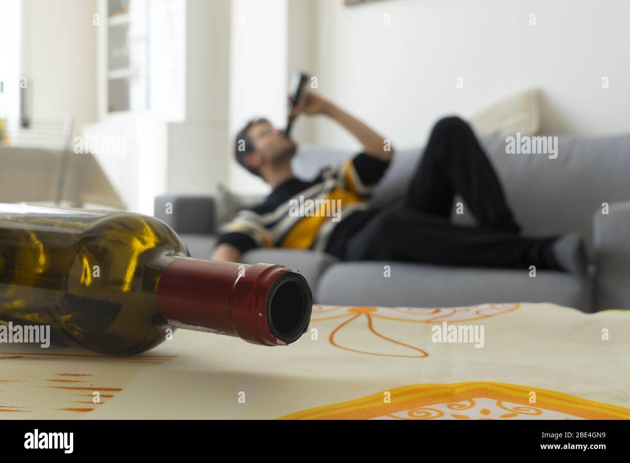 Alkoholiker wird auf dem Sofa zu Hause im Hintergrund betrunken. Leere Flasche Wein im Vordergrund. Familienalkoholismus Konzept. Stockfoto