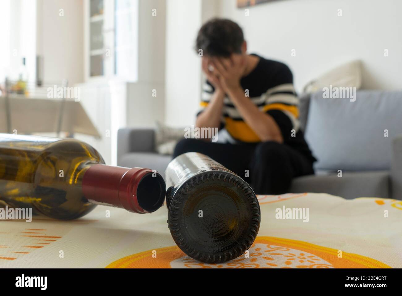 Alkoholiker verzweifelt auf dem Sofa zu Hause. Leere Flasche Wein im Vordergrund. Konzept der Alkoholsucht. Stockfoto