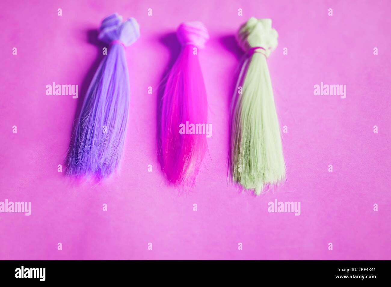 Mehrfarbige gerade lange Haare, Perücken für handgefertigte Puppen auf rosa Hintergrund. Farbige Haarsträhnen. Handarbeit, Hobby, Freizeitkonzept. Draufsicht. Stockfoto