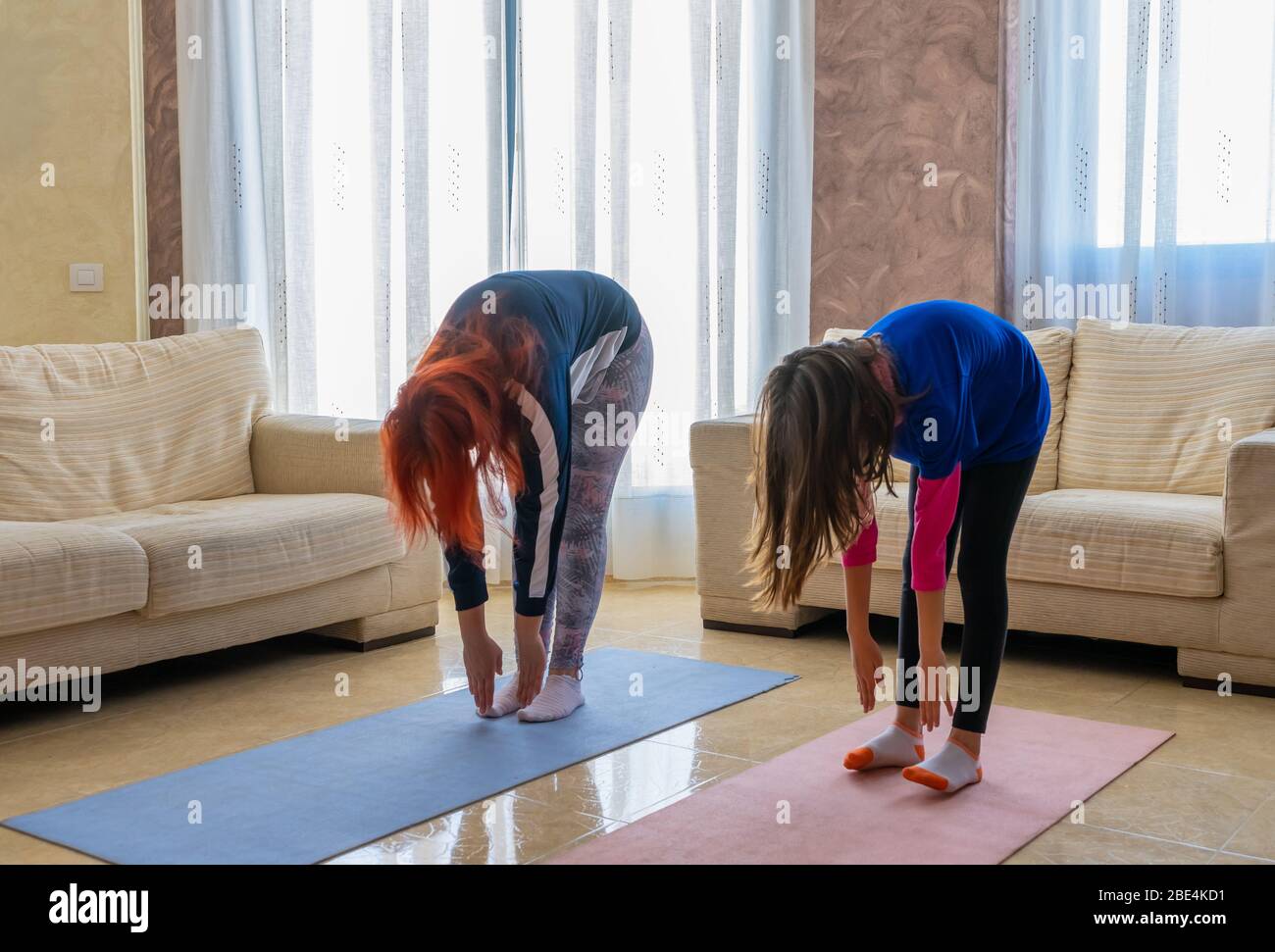 Mutter und Tochter in Sportkleidung Sport unter den weißen Sofas im Wohnzimmer zu Hause. Gesundes Leben Konzept Stockfoto