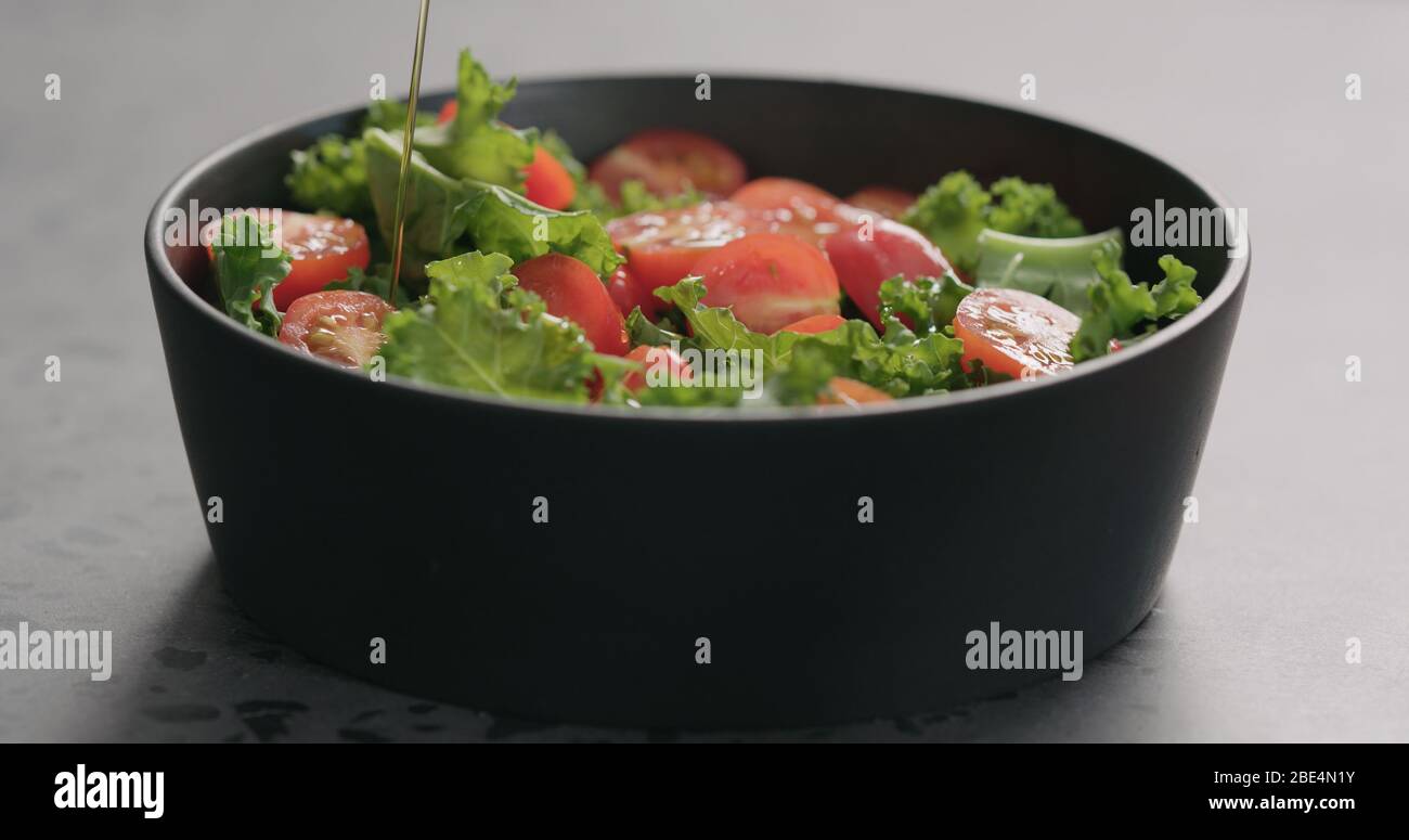 Olivenöl auf Salat mit Tomaten und Grünkohl geben Schwarze Schale auf Betonoberfläche Stockfoto