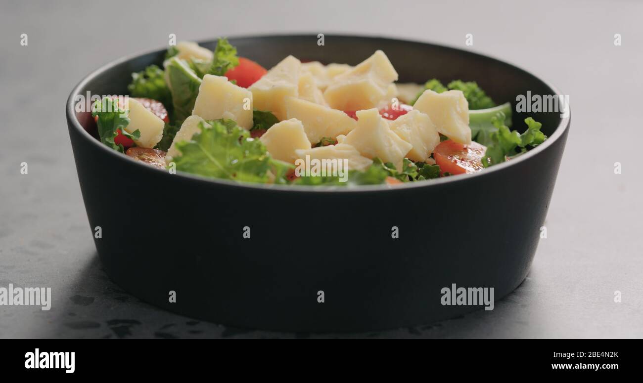 Käse zu Salat mit Tomaten und Grünkohl in schwarzer Schüssel Auf Betonoberfläche Stockfoto