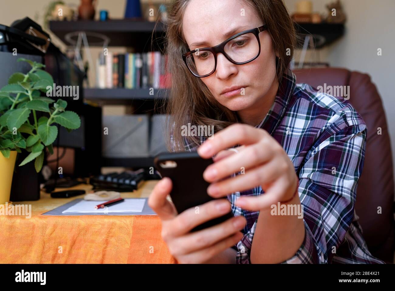 Eine Frau arbeitet zu Hause, liest vom Telefon. Freiberufler. Im Hintergrund ein gemütliches Zimmer. Stockfoto