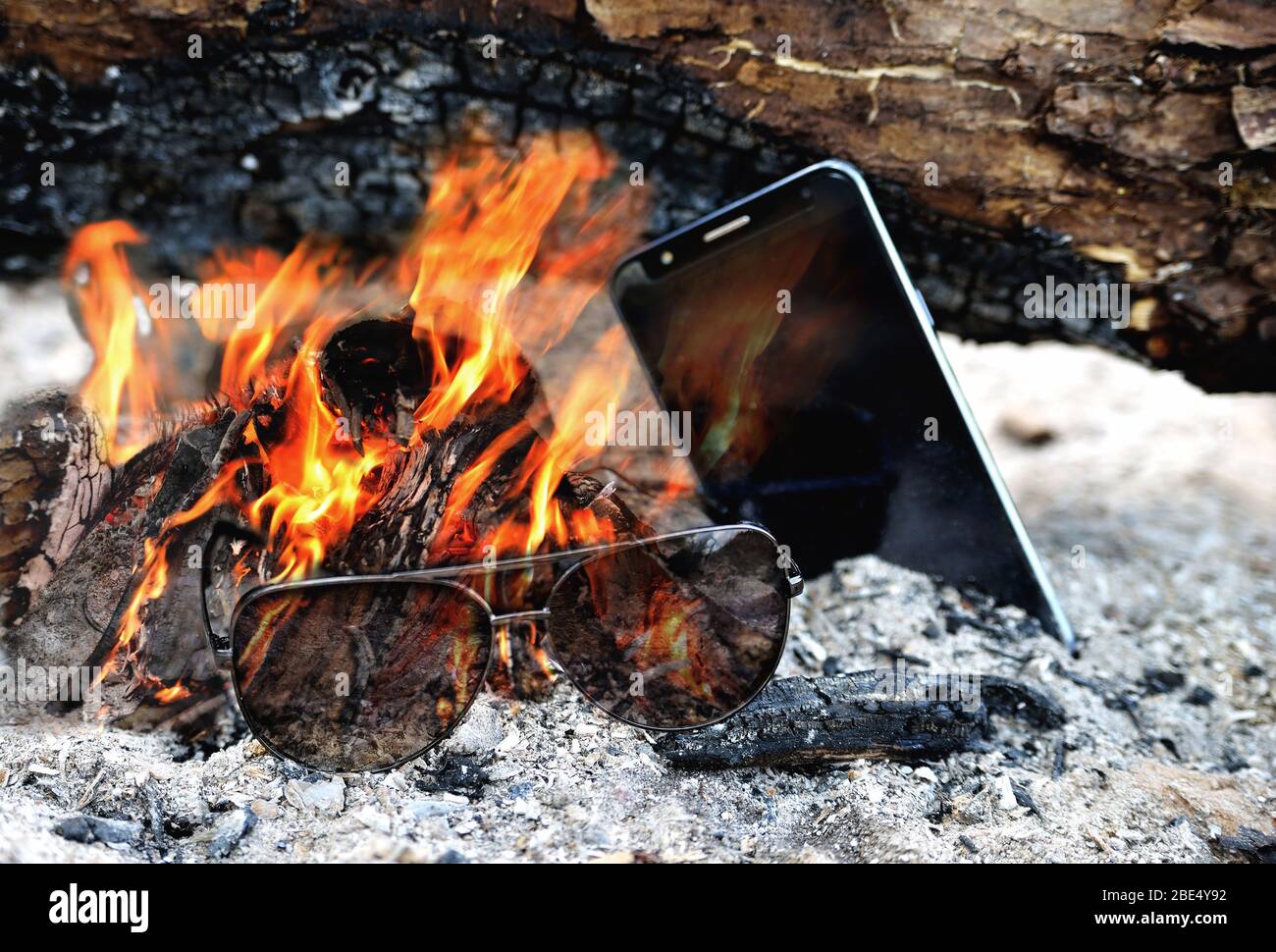 Sonnenbrille und Telefon brennen in der hellen Flamme des Feuers, Esche Brennholz Nahaufnahme Stockfoto