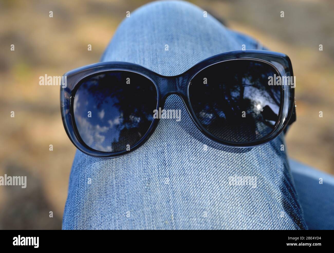 Sonnenbrille am Knie in Jeans, Nahaufnahme Konzept Stockfoto