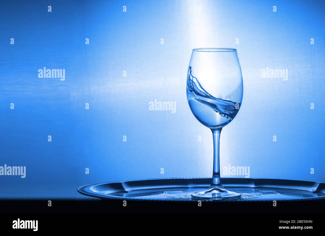 Kaltes transparentes Wasser spritßt aus einem Glas, das auf dem Holztisch in der Nähe bleibt Stockfoto