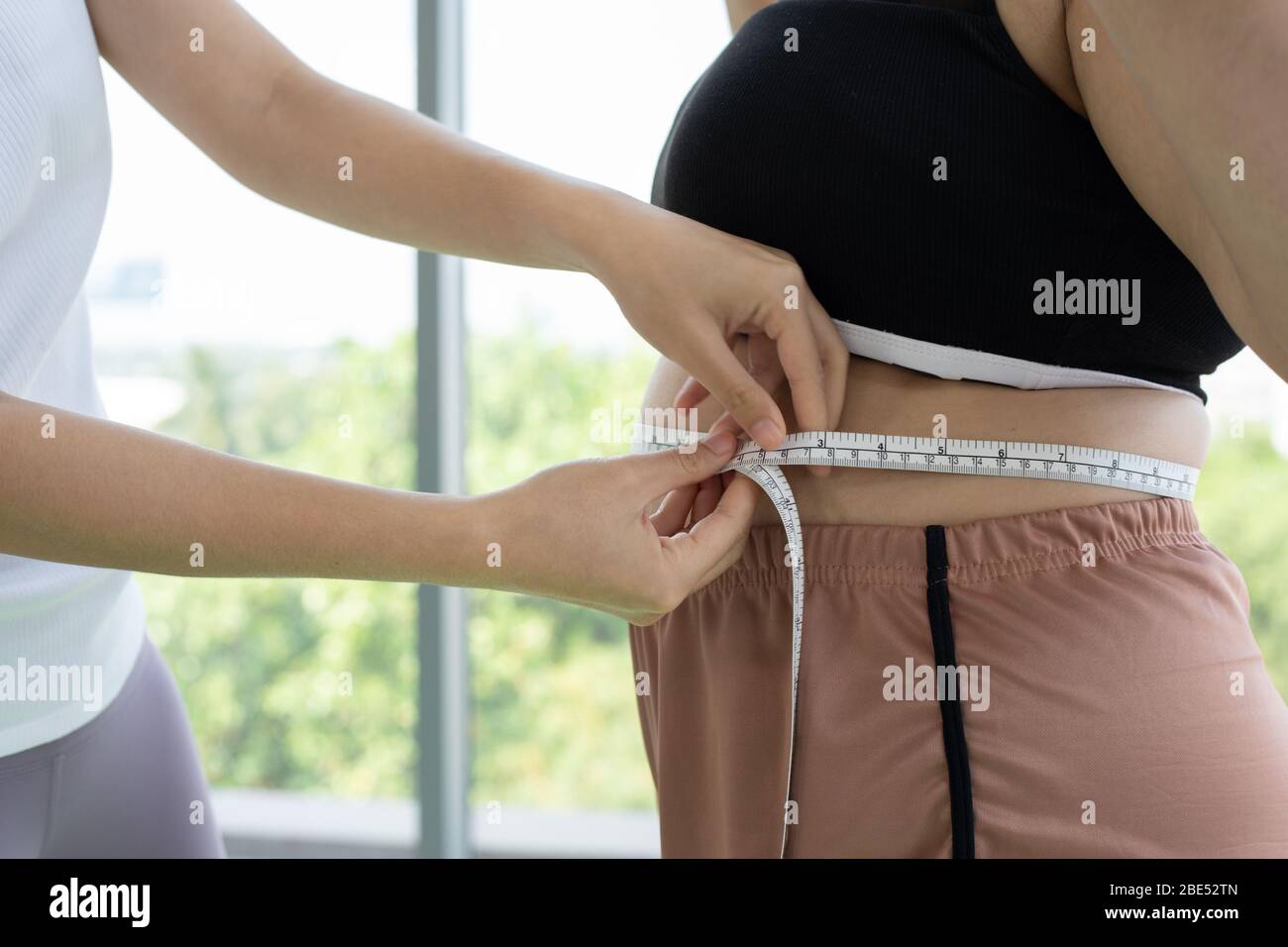 Junge Trainerin misst Fettschicht übergewichtiger Frau mit Weste im Fitnessbereich Stockfoto