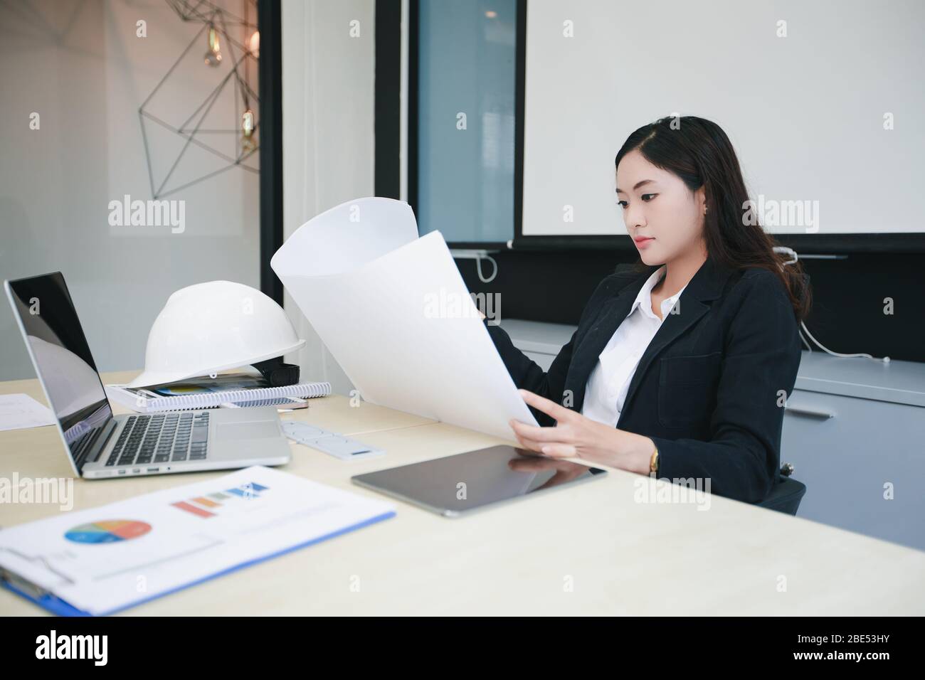 Asiatische Frauen Engineering hält Blaupausen und haben einen Hut auf dem Tisch für die Arbeit im Büro Stockfoto