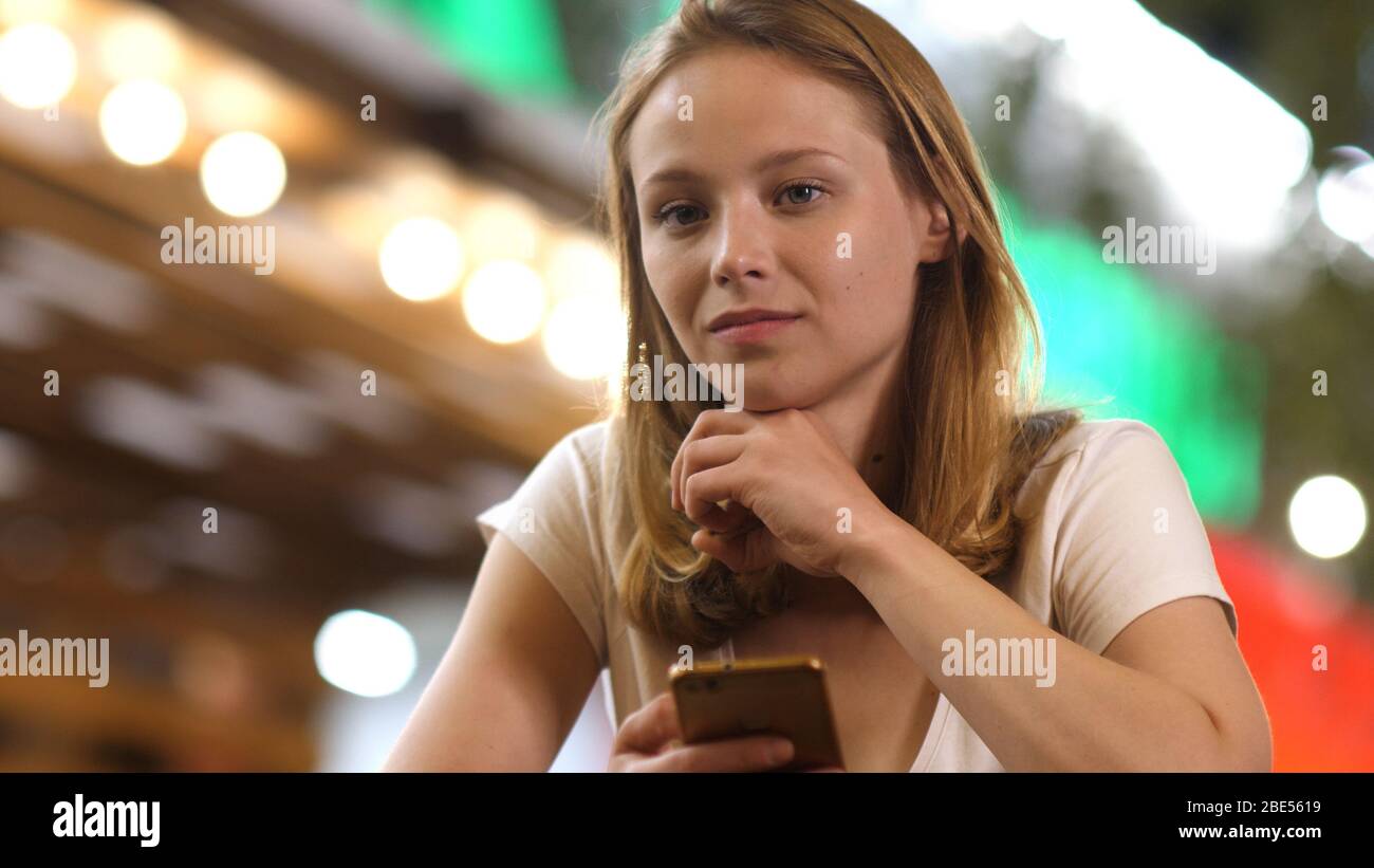 Angespanntes Teenager-Mädchen, das die Kamera anschaut und ein Telefon in der Hand hält. Stockfoto