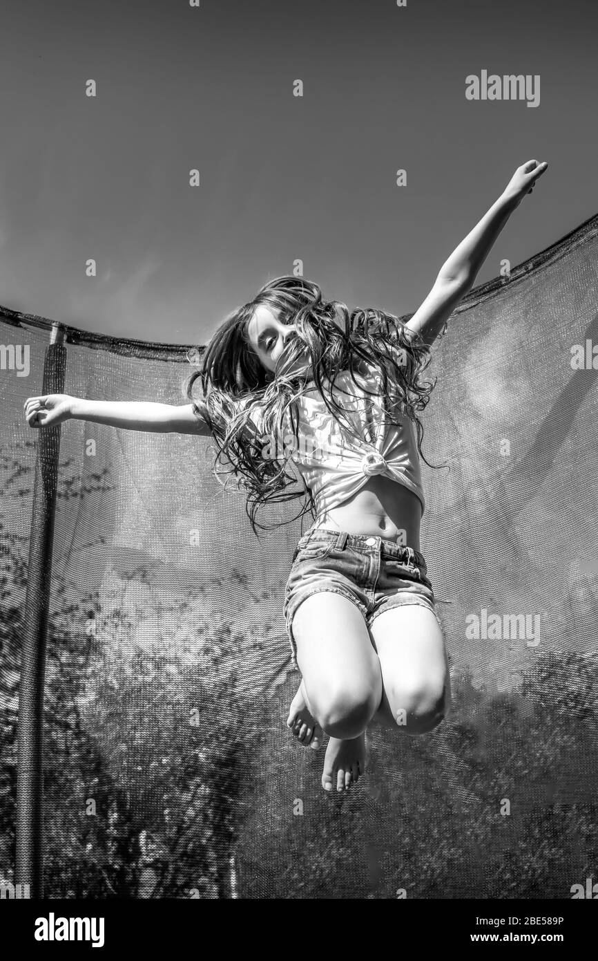 Junges Mädchen, das Spaß in der Sonne hat, fliegen und auf einem Trampolin hüpfen, um etwas Bewegung zu bekommen Stockfoto