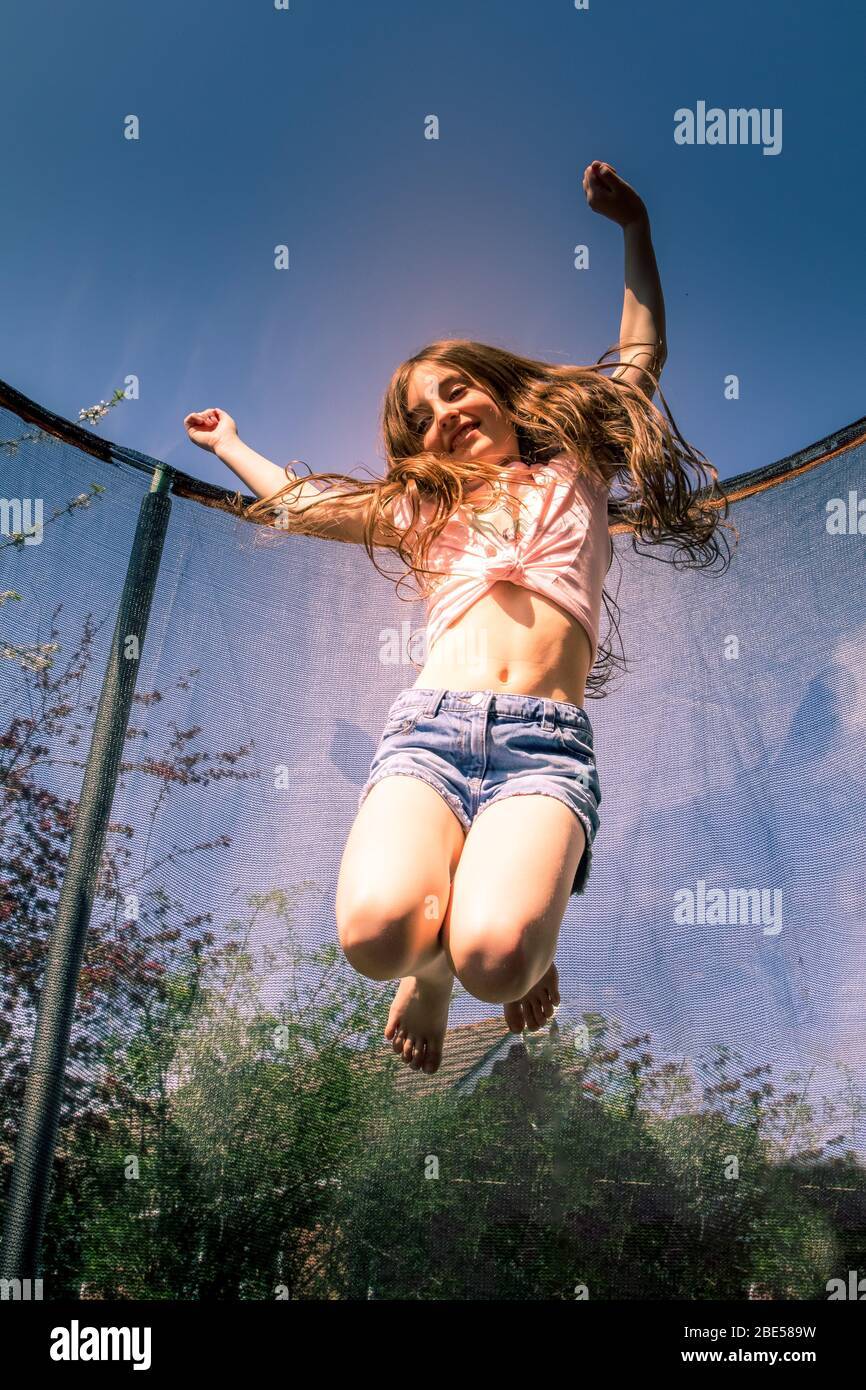 Junges Mädchen, das Spaß in der Sonne hat, fliegen und auf einem Trampolin hüpfen, um etwas Bewegung zu bekommen Stockfoto