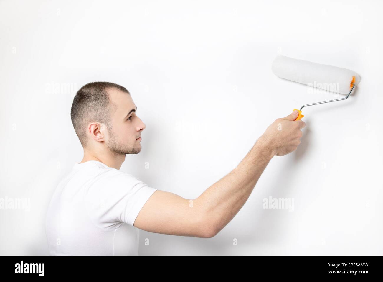 Ein Typ in einem weißen T-Shirt malt mit einer Farbwalze eine Wand. Stockfoto