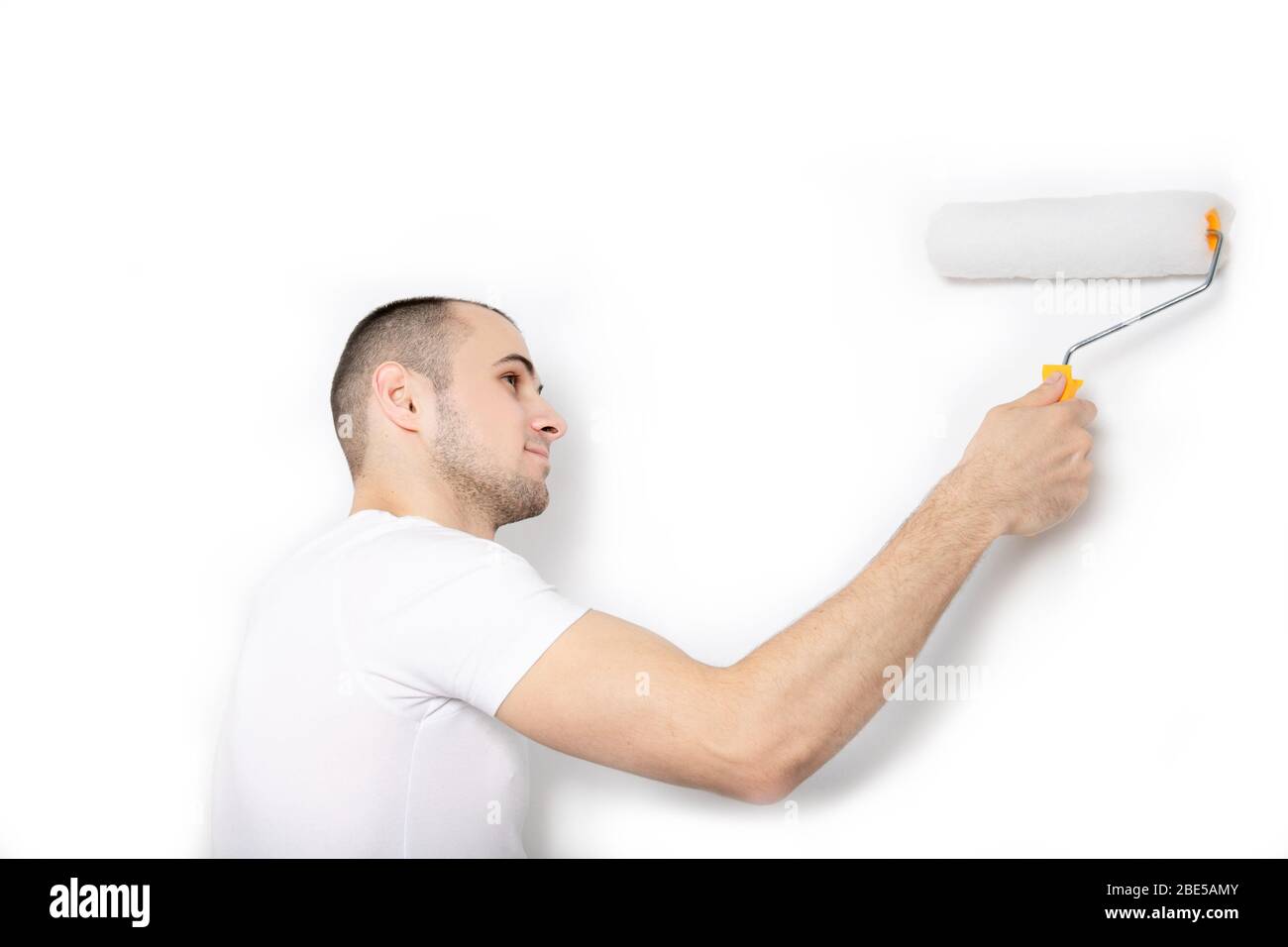 Ein Typ in einem weißen T-Shirt malt mit einer Farbwalze eine Wand. Stockfoto