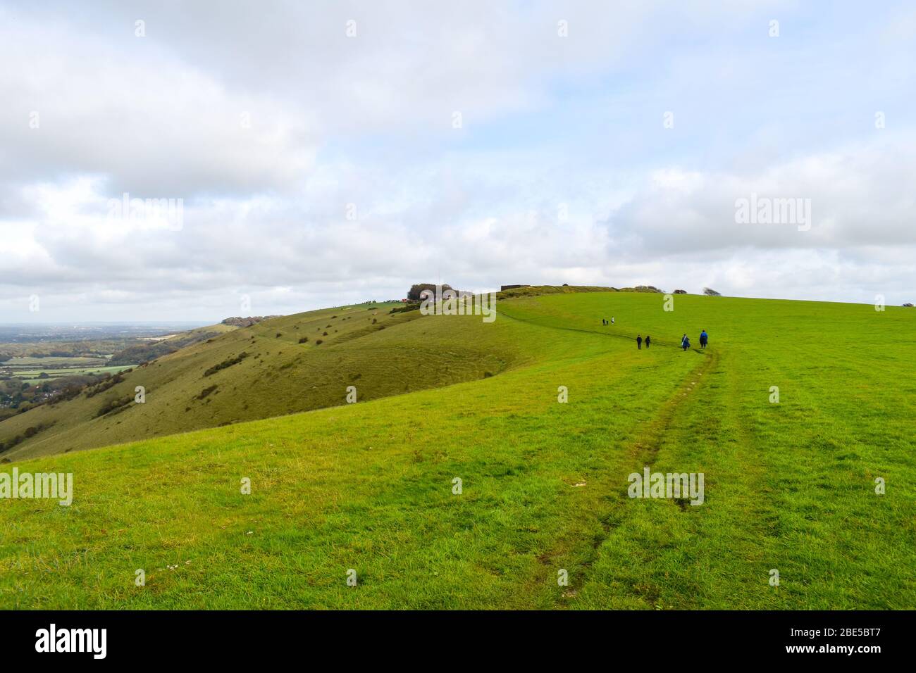 Menschen, die auf dem South Downs Way-Wanderweg am Devils Dyke in Sussex, Großbritannien, wandern. Die Landschaft ist sanft grüne Hügel an einem bewölkten Tag. Stockfoto