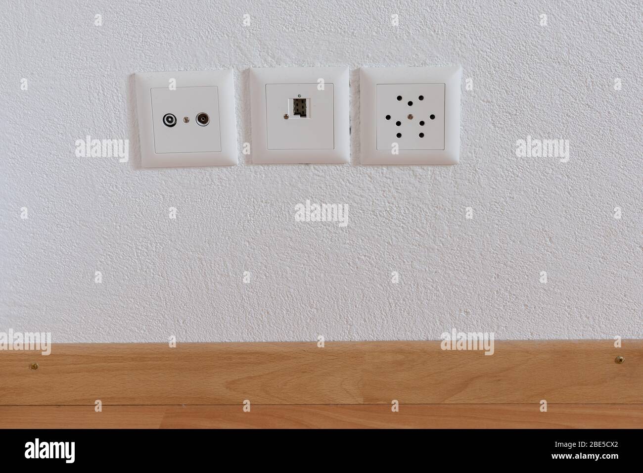 Eine Nahaufnahme der Steckdosen für Fernsehen, Internet, Telefon und Strom auf einer weißen Gipswand und Holzboden Stockfoto