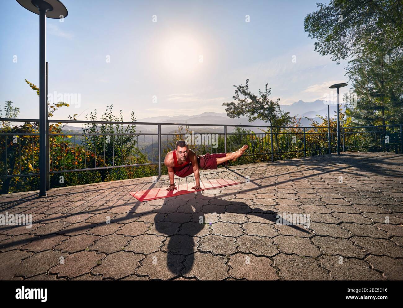 Passen Mann im roten Kostüm Yoga bakasana Stellen im Park mit Bergblick in Almaty, Kasachstan Stockfoto