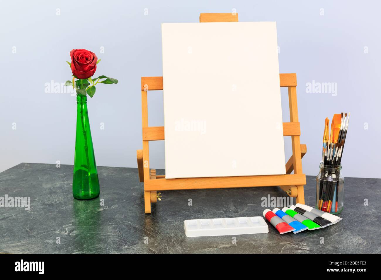 Künstlerleinwand auf einer Tischstaffel, die bereit ist, ein Stillleben-Motiv einer grünen Flasche mit Rosenblütenkopf zu malen Stockfoto