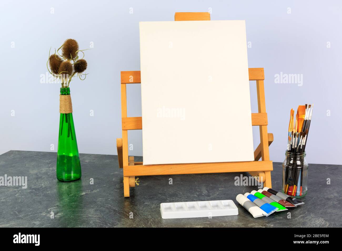 Künstlerleinwand auf einer Desktop-Staffelei bereit, ein Stillleben Thema einer grünen Flasche mit Teelöffel Seed Heads malen Stockfoto