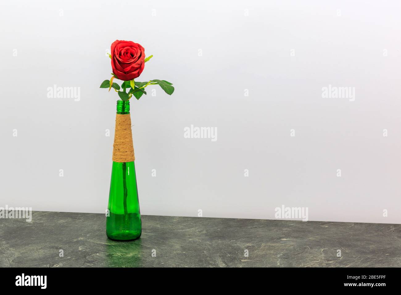 Einzelne rote Rose in einer großen grünen Flasche mit hellblauem Hintergrund Stockfoto