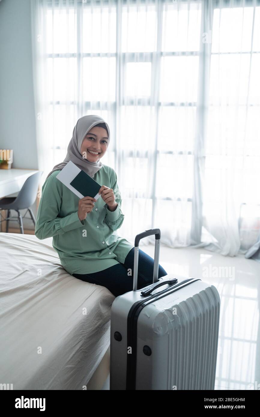 asiatische muslimische Frau lächeln mit einem Ticket und Koffer im Schlafzimmer Stockfoto asiatische muslimische Frau lächeln mit einem Ticket und Koffer im Schlafzimmer Stockfoto